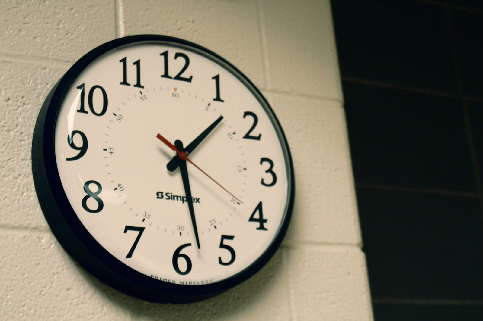 Reloj redondo de pared con la esfera negra sobre una pared de ladrillo blanco